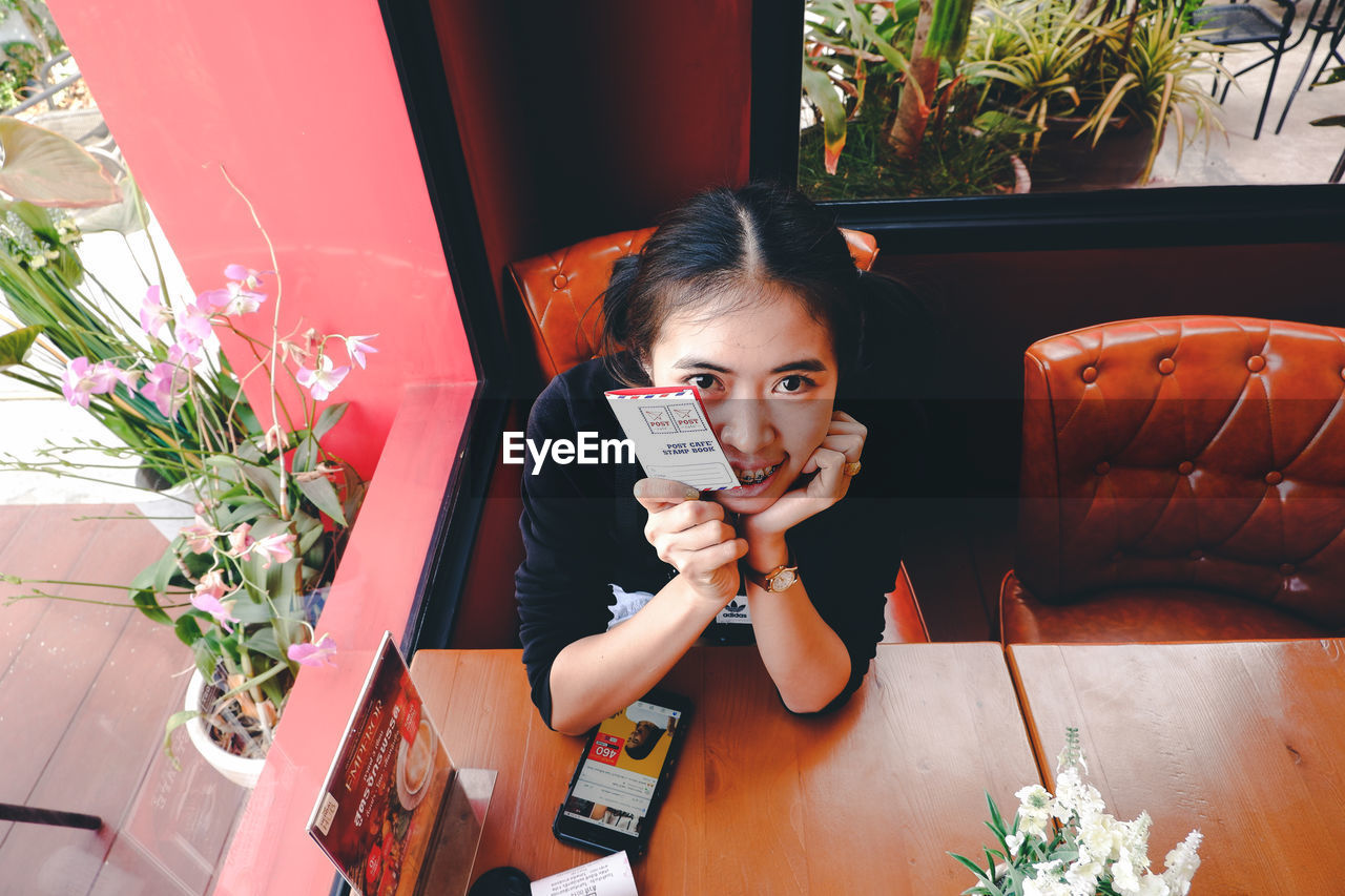 PORTRAIT OF YOUNG WOMAN SITTING ON POTTED PLANT