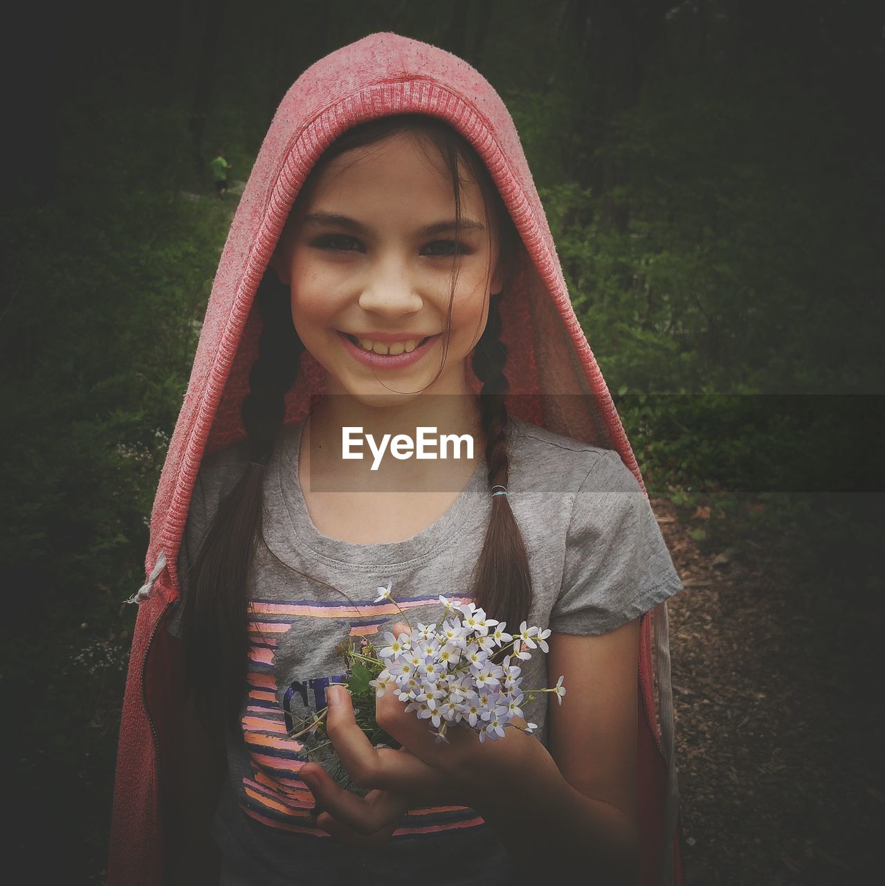 Portrait of girl smiling while holding flowers against plants