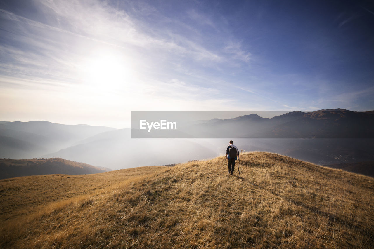 Rear view of male backpacker walking on mountain against sky