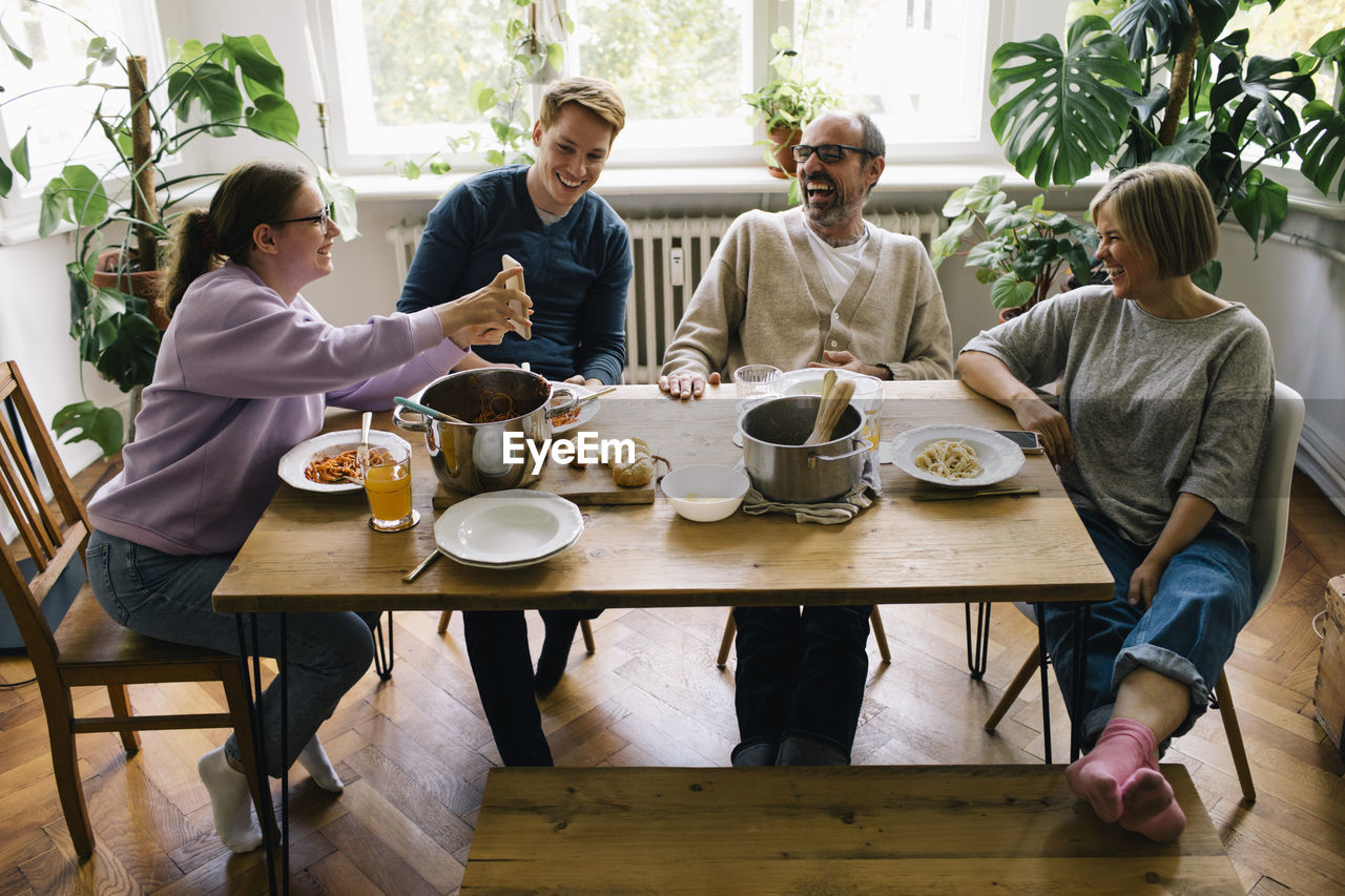 Happy family enjoying while sharing smart phones sitting at dining table in home