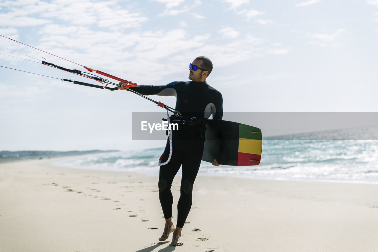 Man with kiteboard standing at beach