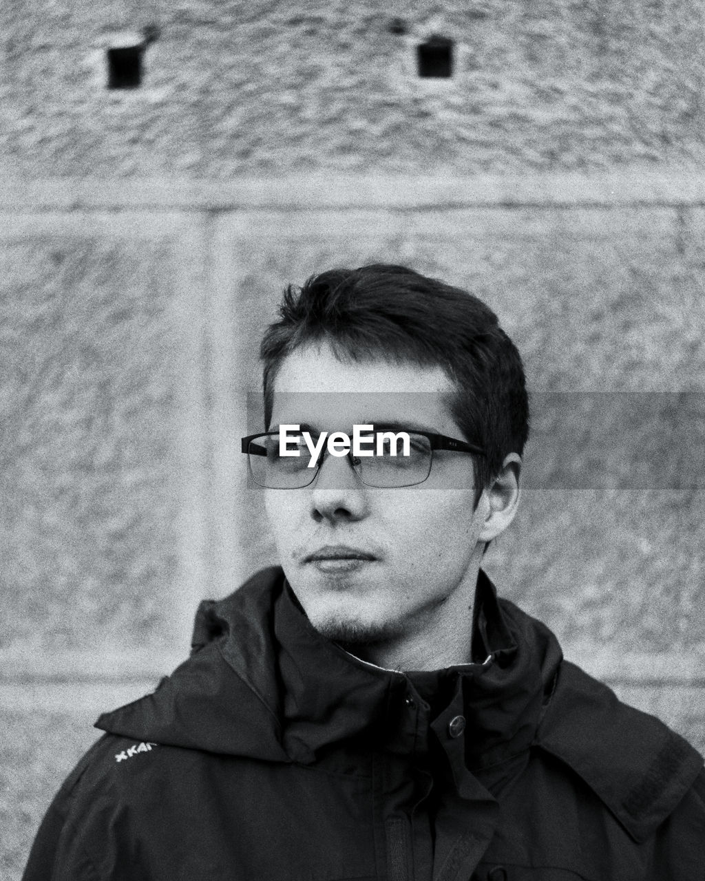 Thoughtful young man wearing eyeglasses looking away against wall