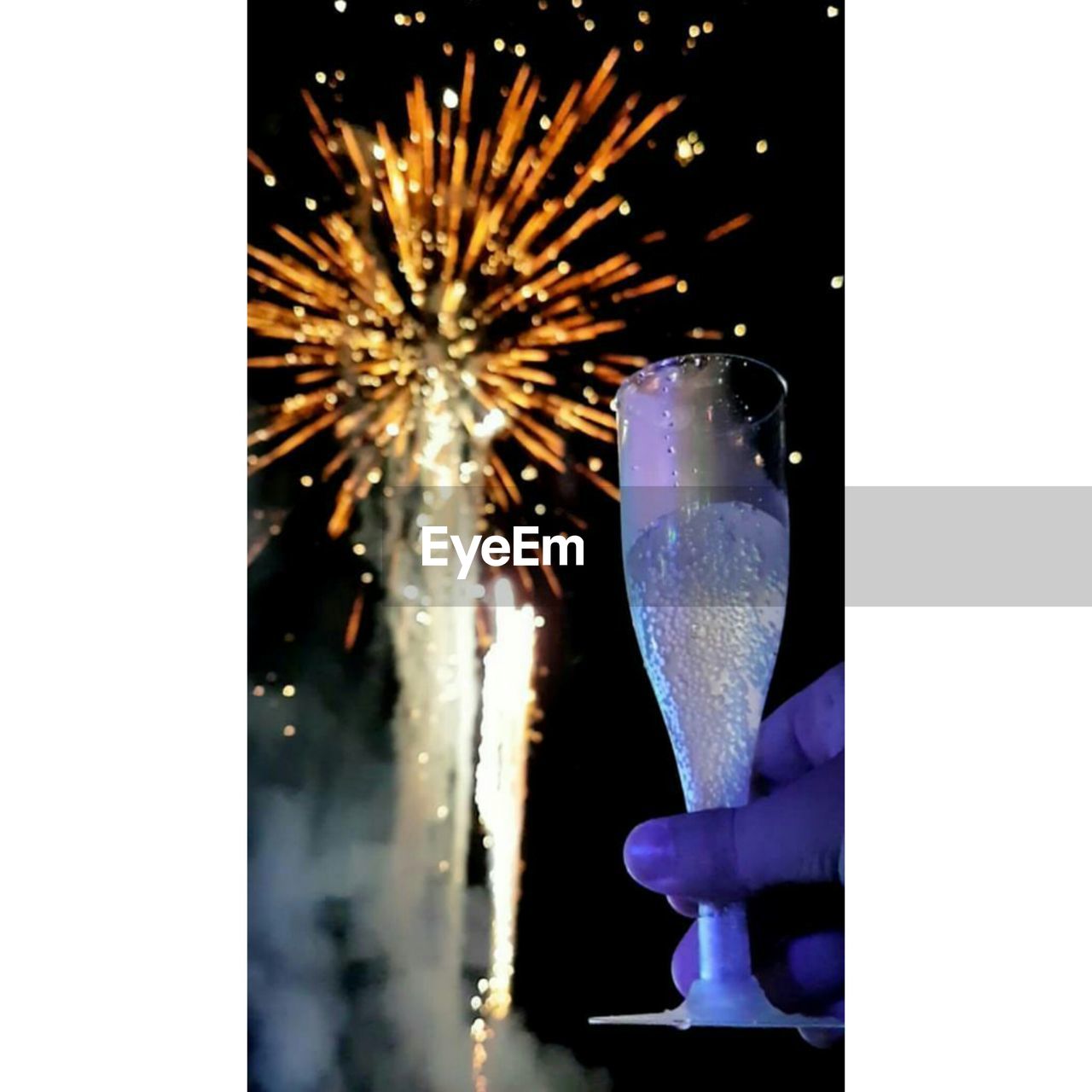 Cropped hand of person holding champagne flute against illuminated firework display at night