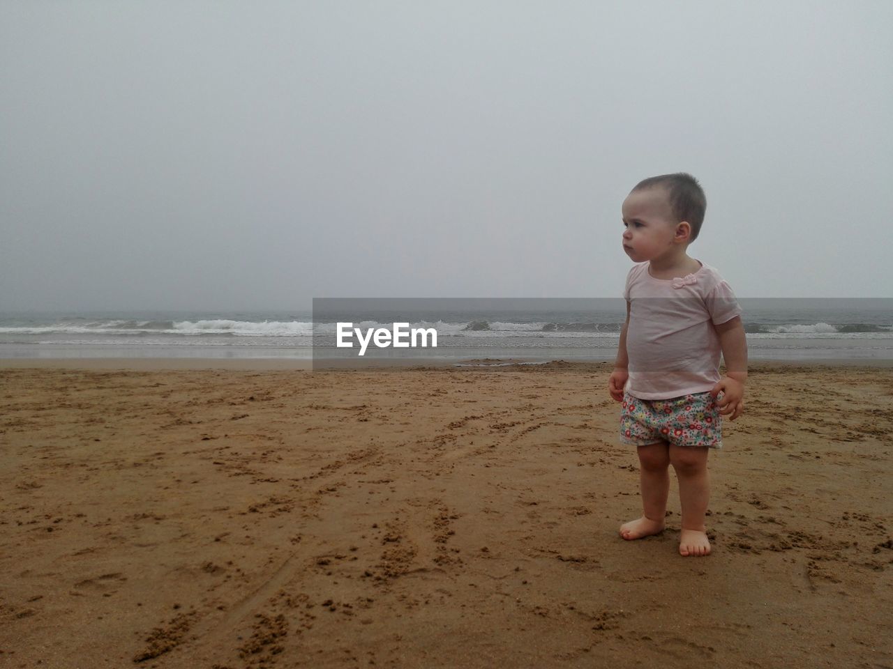 Baby girl looking away while standing at beach