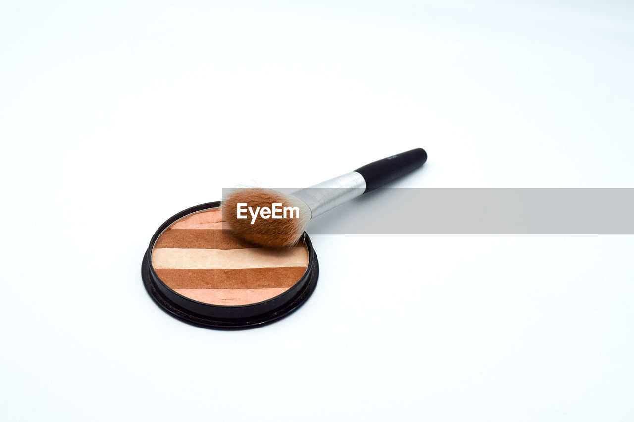 Close-up of make-up with brush over white background