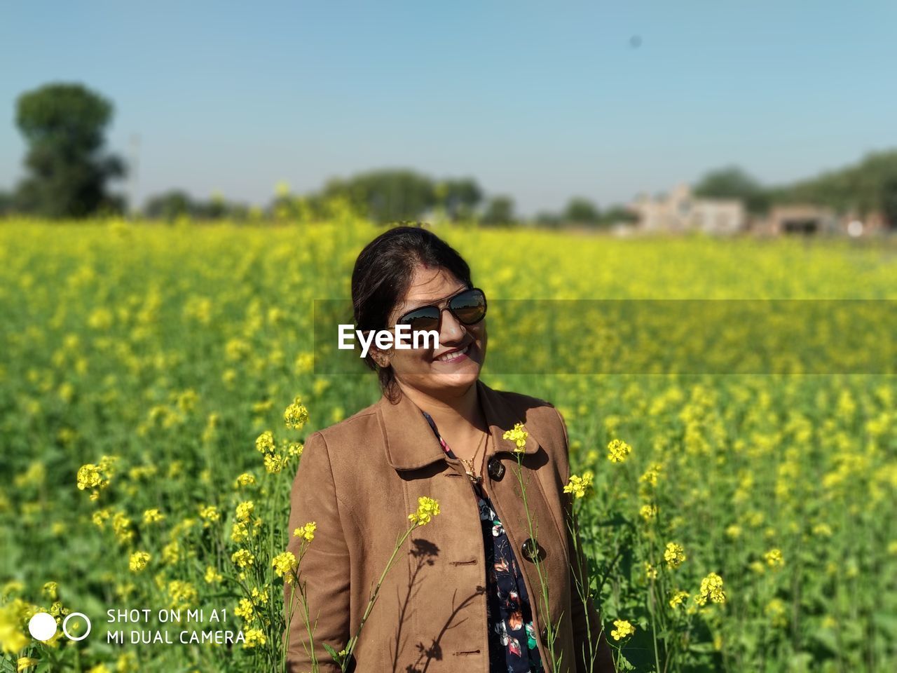 PORTRAIT OF YOUNG WOMAN STANDING BY YELLOW FLOWERS