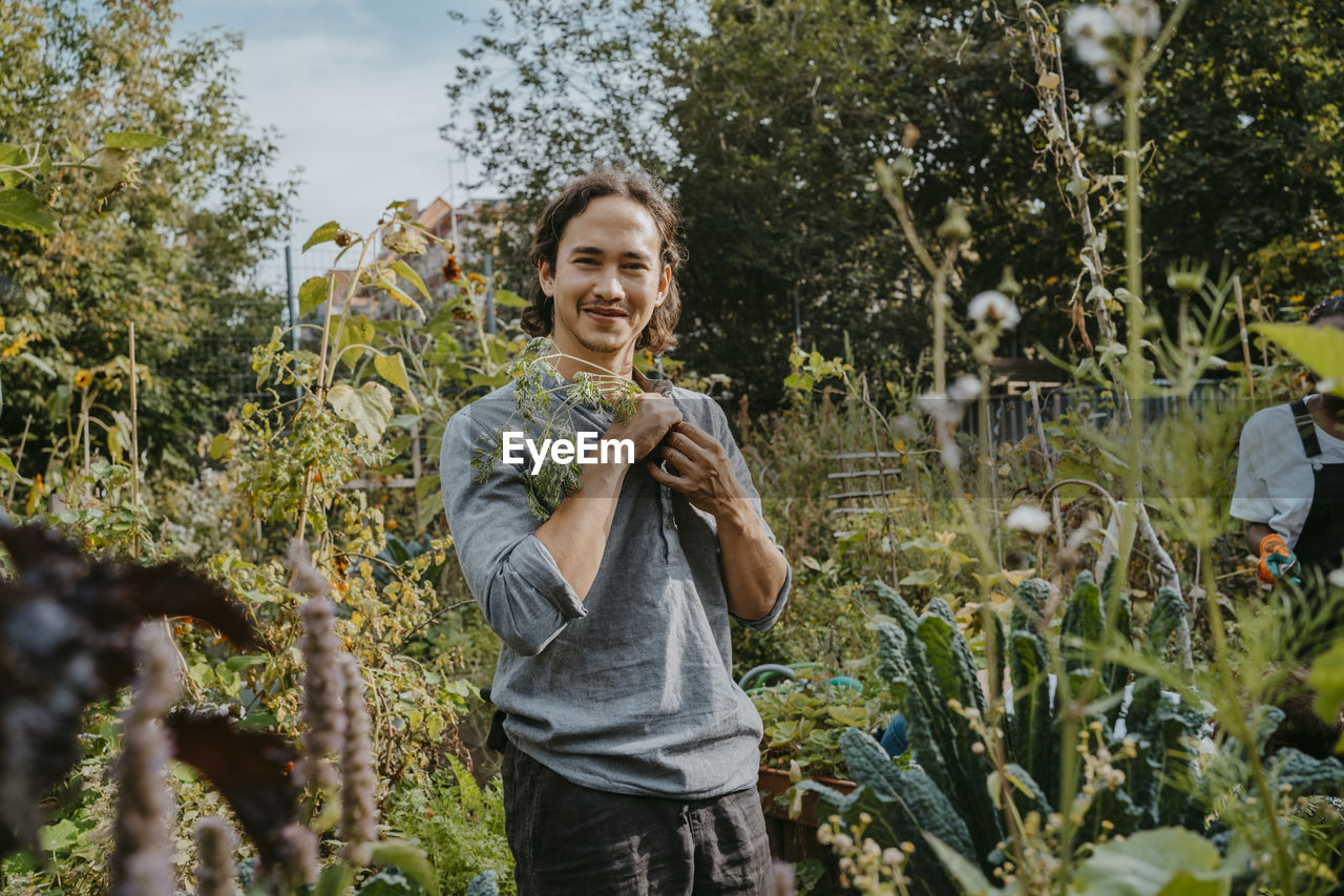 Portrait of smiling male agricultural shareholder with plant in urban garden