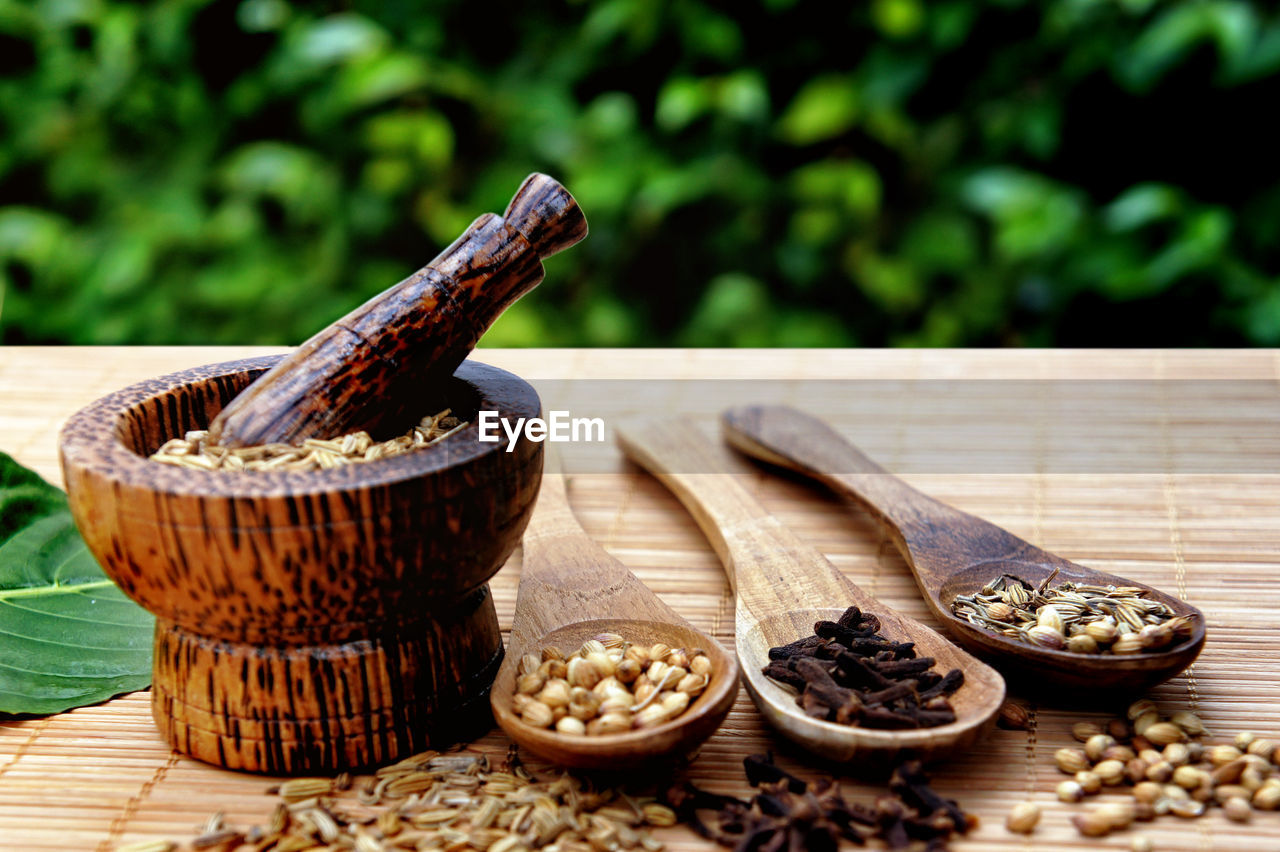 Close-up of spices and herbs with mortar and pestle by wooden spoons on table