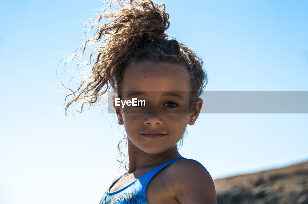 Portrait of confident girl with curly hair standing against clear sky