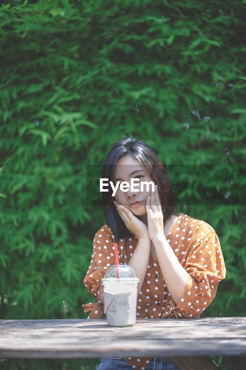 PORTRAIT OF A BEAUTIFUL YOUNG WOMAN DRINKING WATER FROM TABLE