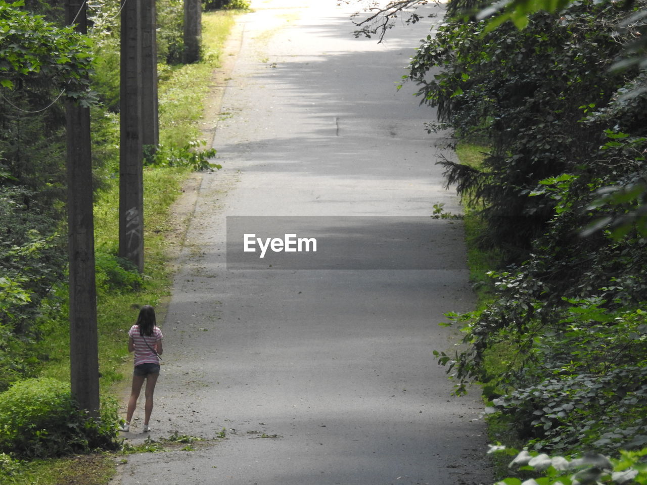 REAR VIEW OF WOMAN WALKING ON FOOTPATH BY ROAD