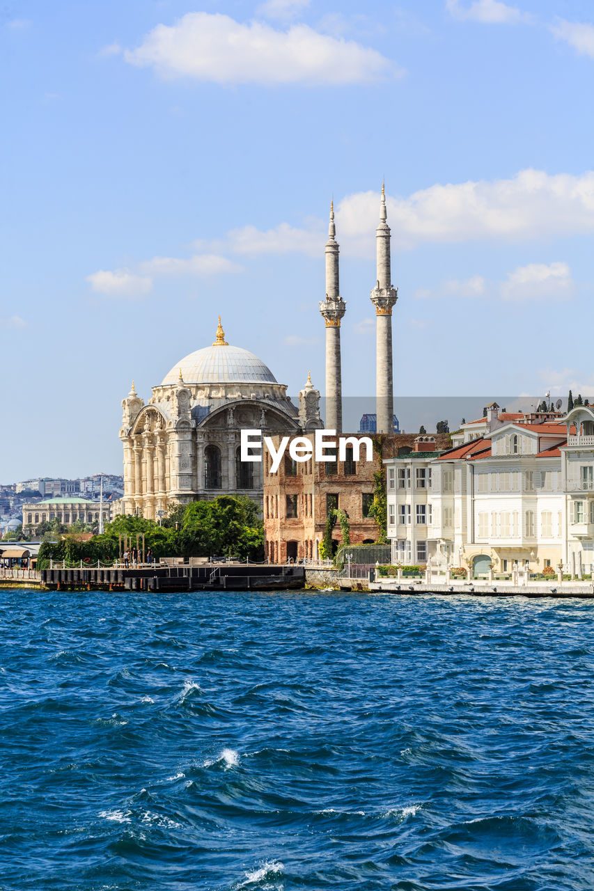 View of buildings at waterfront against cloudy sky