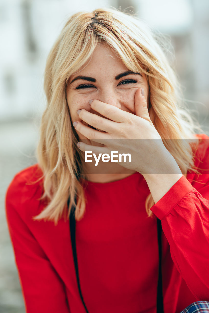 Portrait of cheerful young woman covering mouth