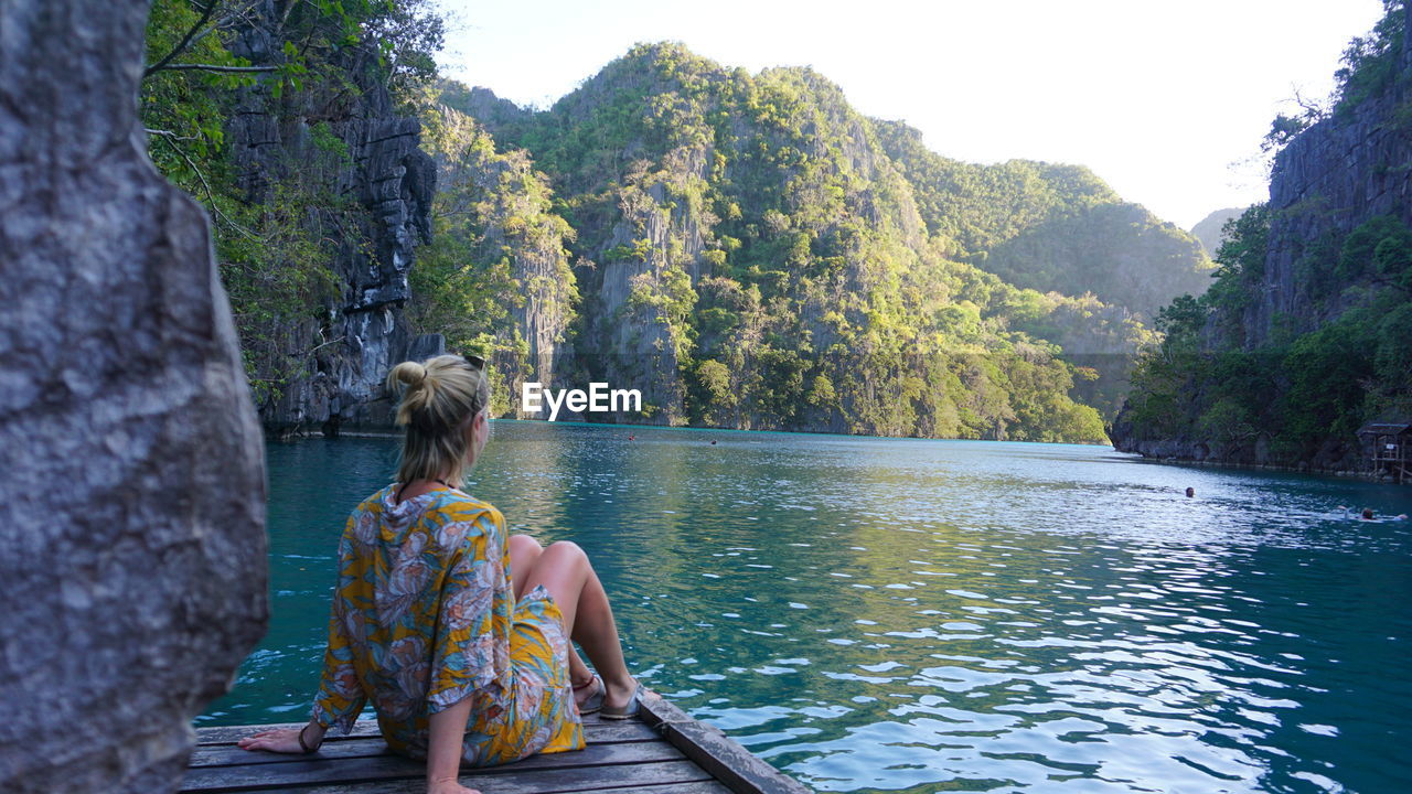 REAR VIEW OF WOMAN SITTING BY LAKE