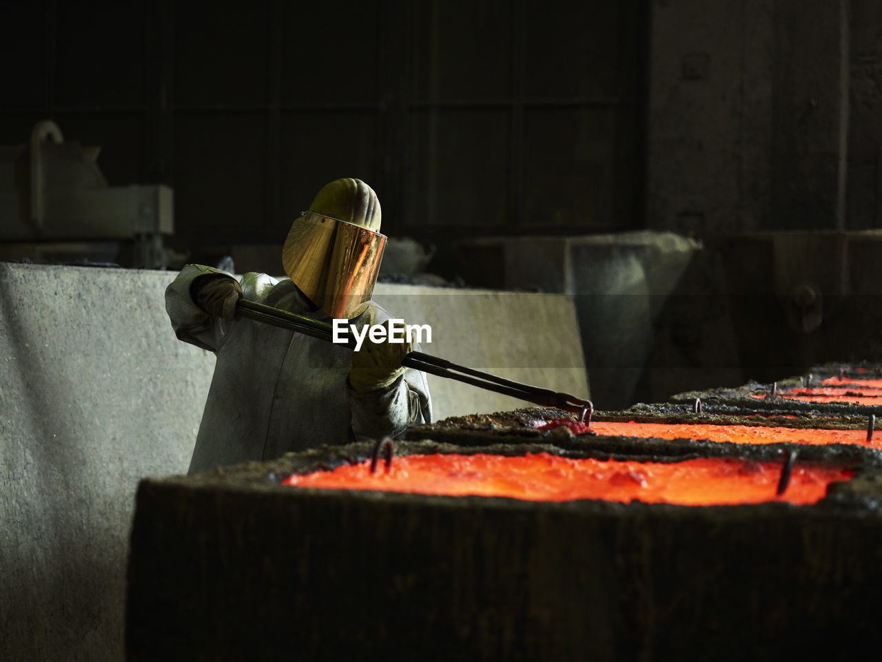 Industry, worker checking liquid copper in casting moulds with pliers