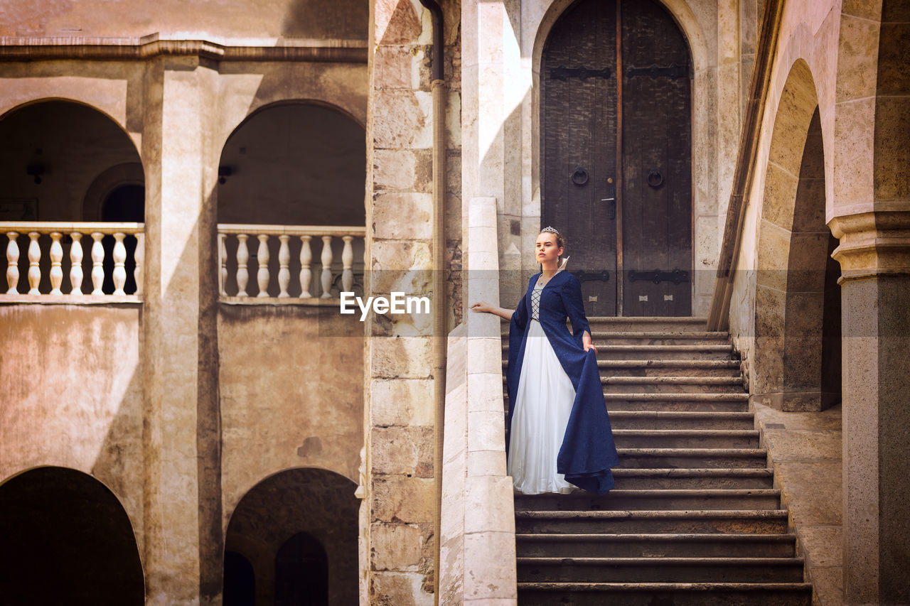 Young beautiful princess or queen standing on steps of medieval castle