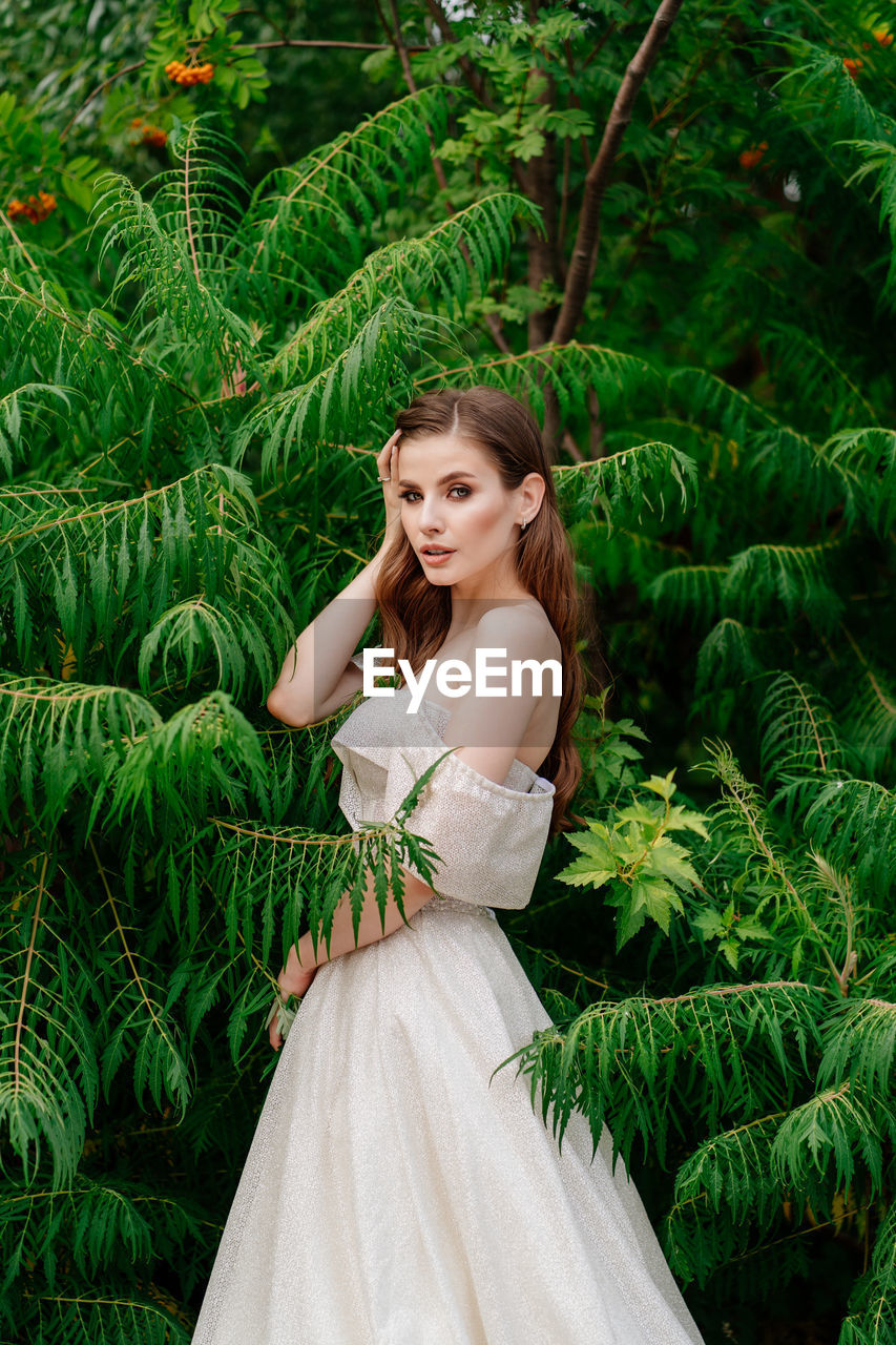 PORTRAIT OF BEAUTIFUL WOMAN STANDING AGAINST PLANTS