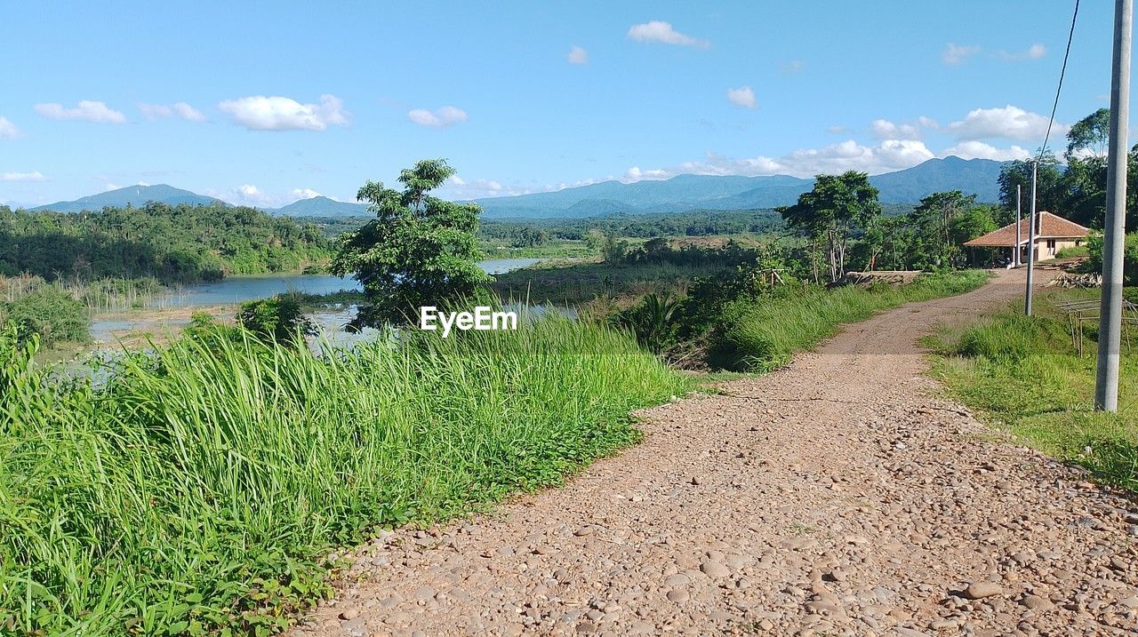 sky, plant, landscape, nature, environment, scenics - nature, rural area, agriculture, soil, land, cloud, mountain, field, road, beauty in nature, no people, tree, rural scene, tranquility, green, grass, day, tranquil scene, transportation, growth, footpath, outdoors, the way forward, dirt road, non-urban scene, mountain range, water, dirt, trail, blue, travel, crop