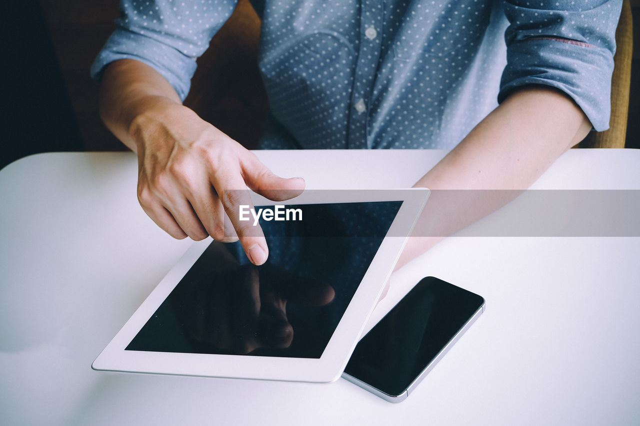 Midsection of man using digital tablet at table