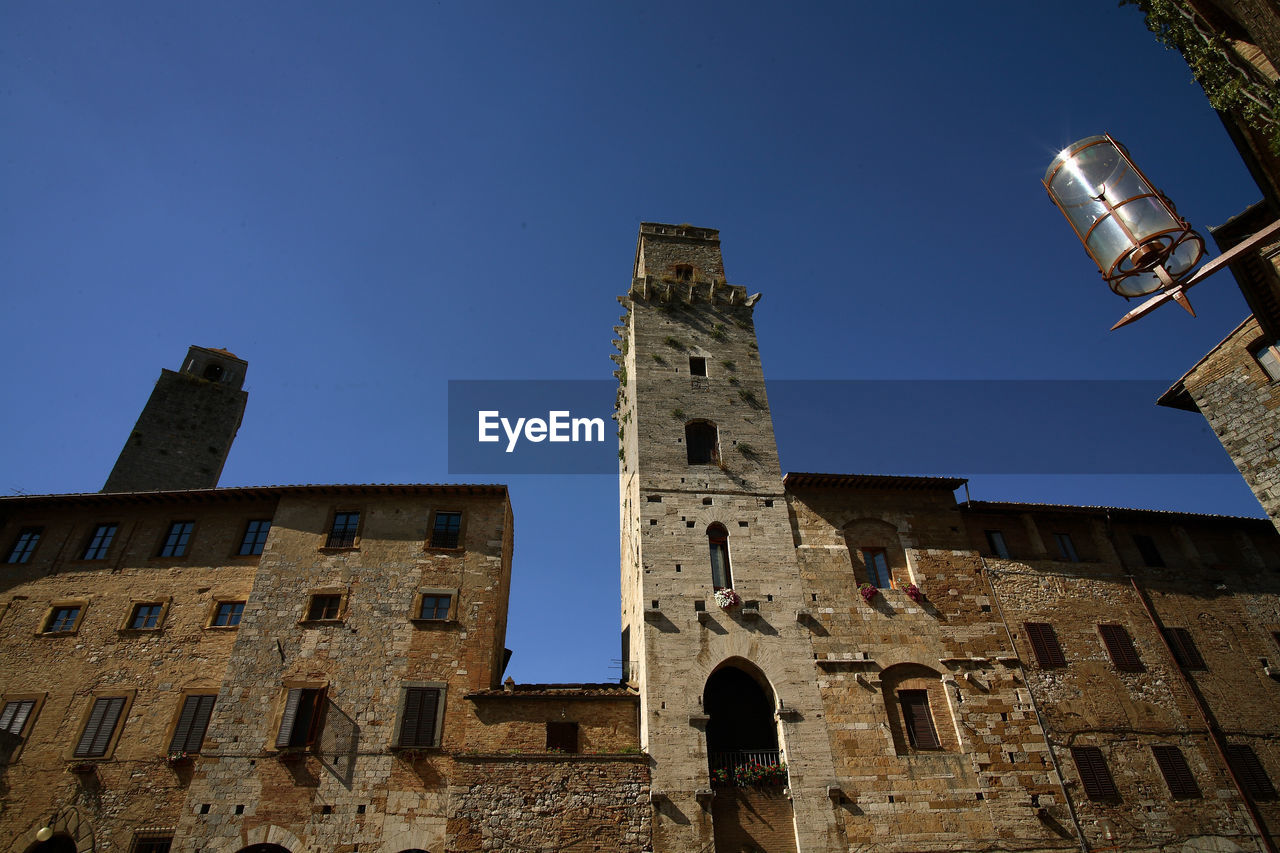 Low angle view of historic building against blue sky, san geminiano, tuscany, italy