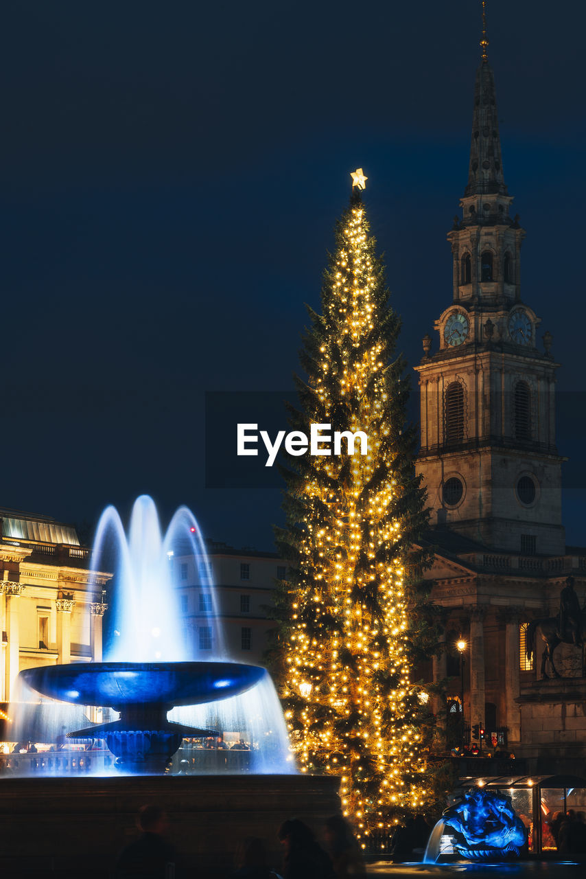 Low angle view of illuminated building, fountain and christmas tree against sky at night