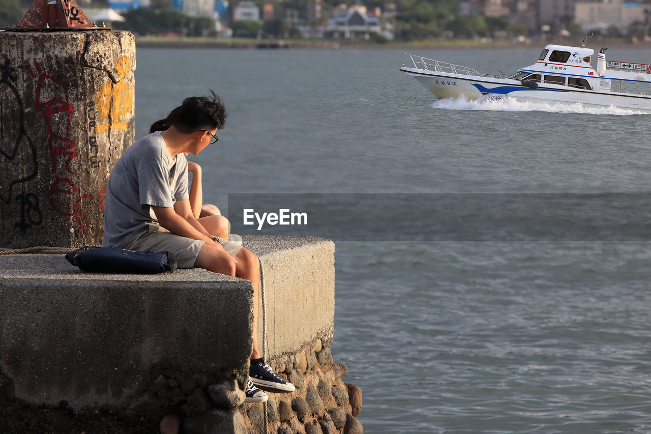 SIDE VIEW OF MAN SITTING ON BOAT