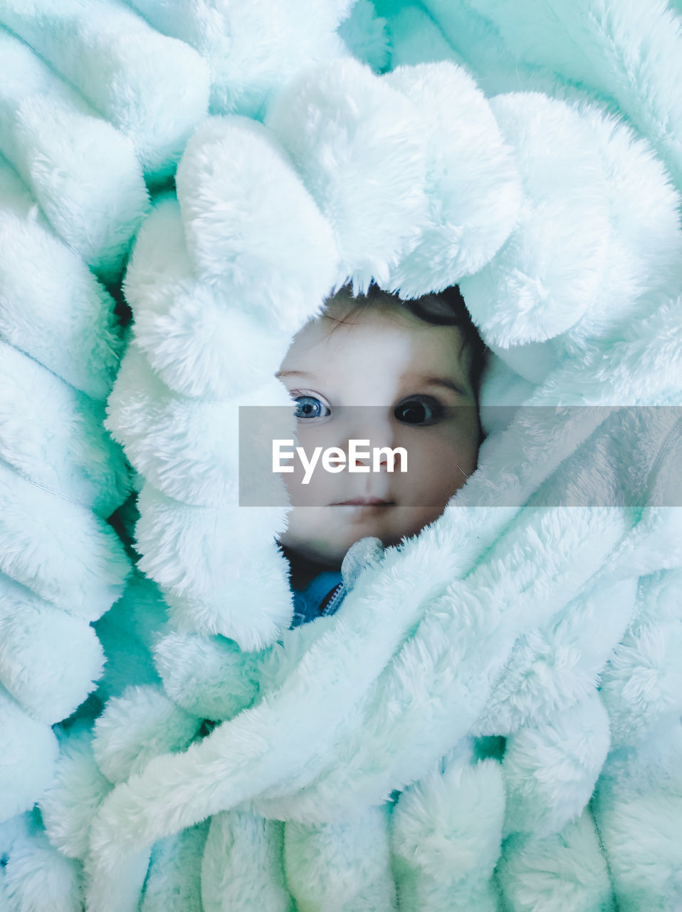 Portrait of cute baby lying on bed wrapped in blanket