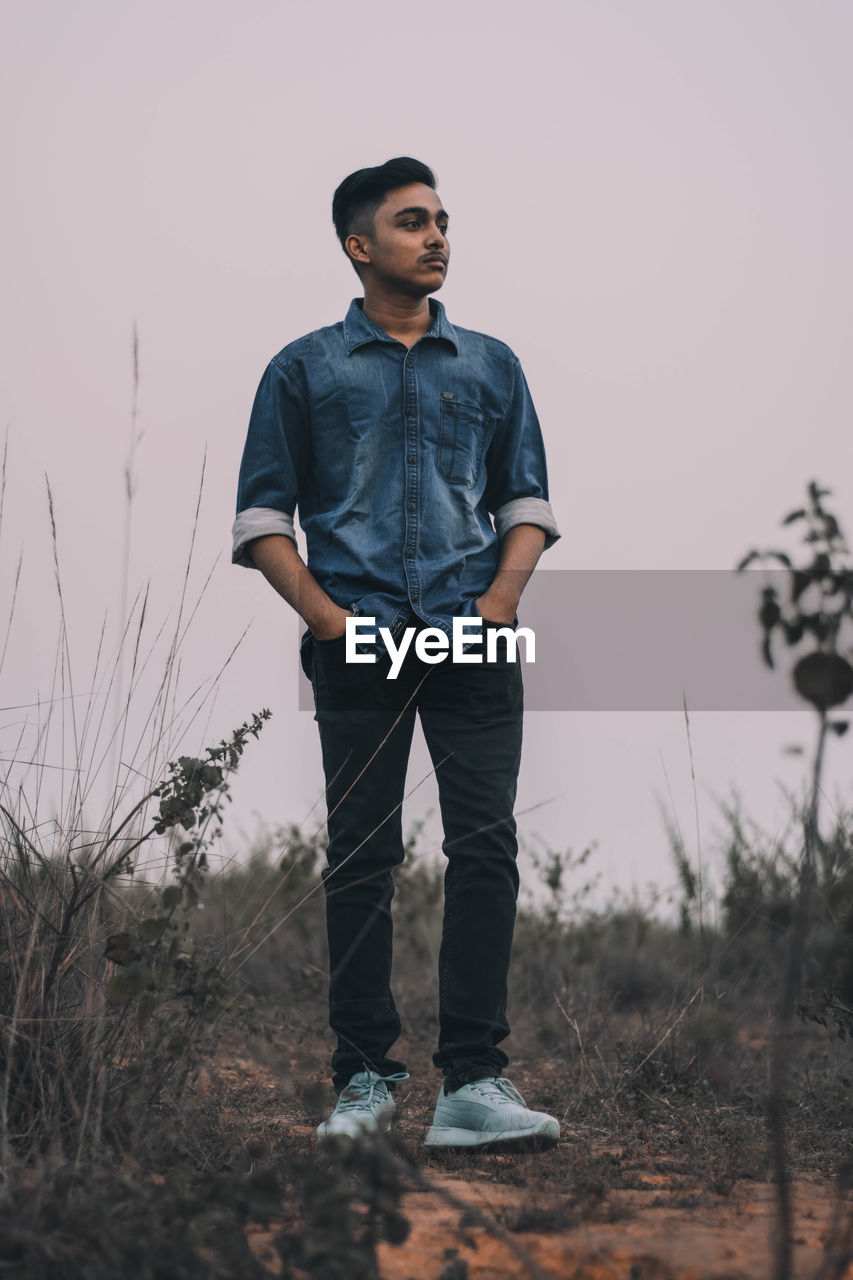 Full length of thoughtful young man standing on field