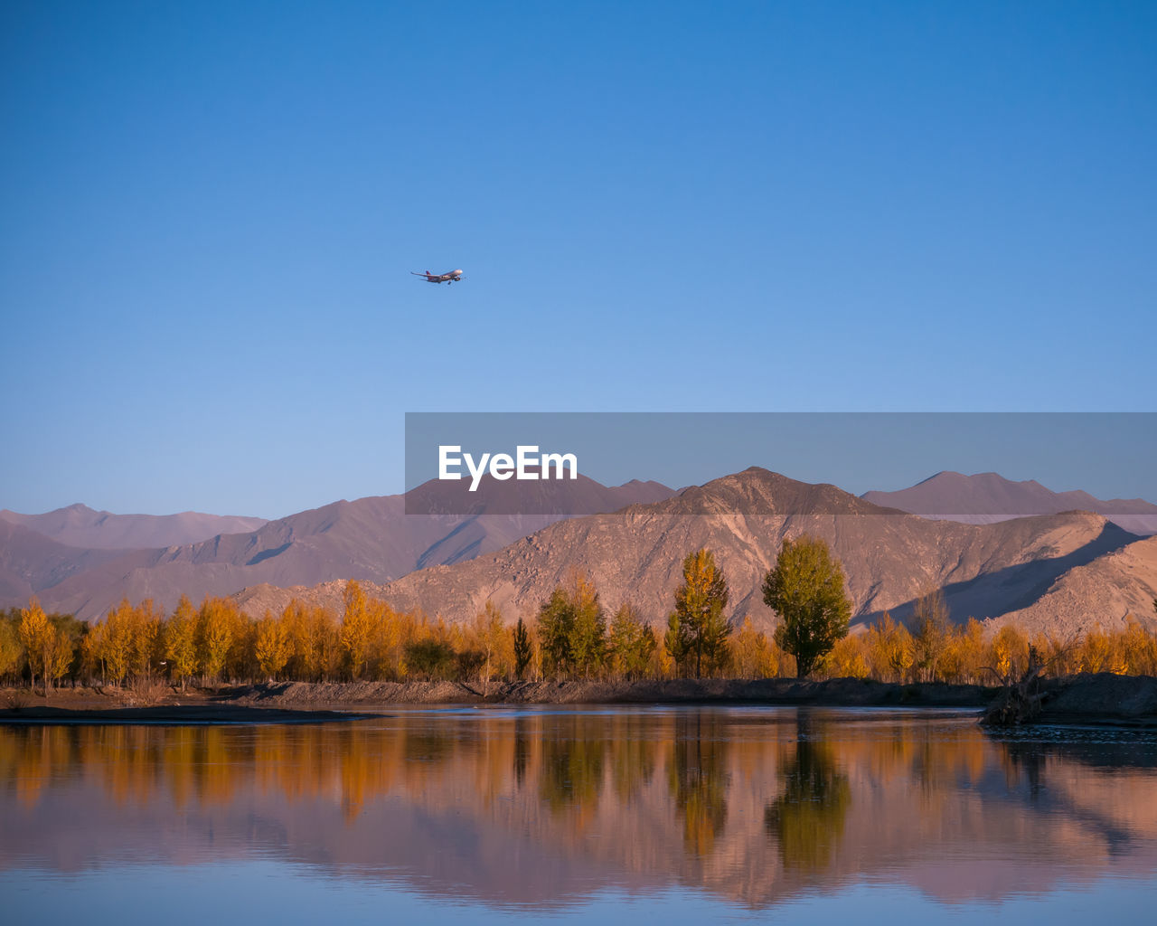 A plane is flying over mountains and rivers at sunrise.