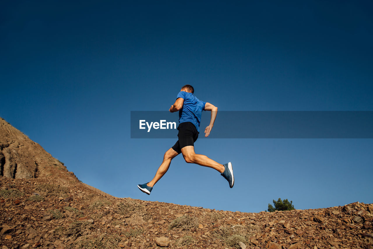 Low angle view of man jumping against clear blue sky