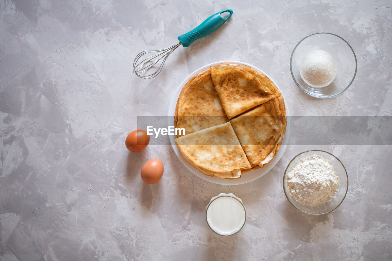 Top view of raw brown eggs, flour, milk, sugar and whisk as ingredients of batter or dough pancakes
