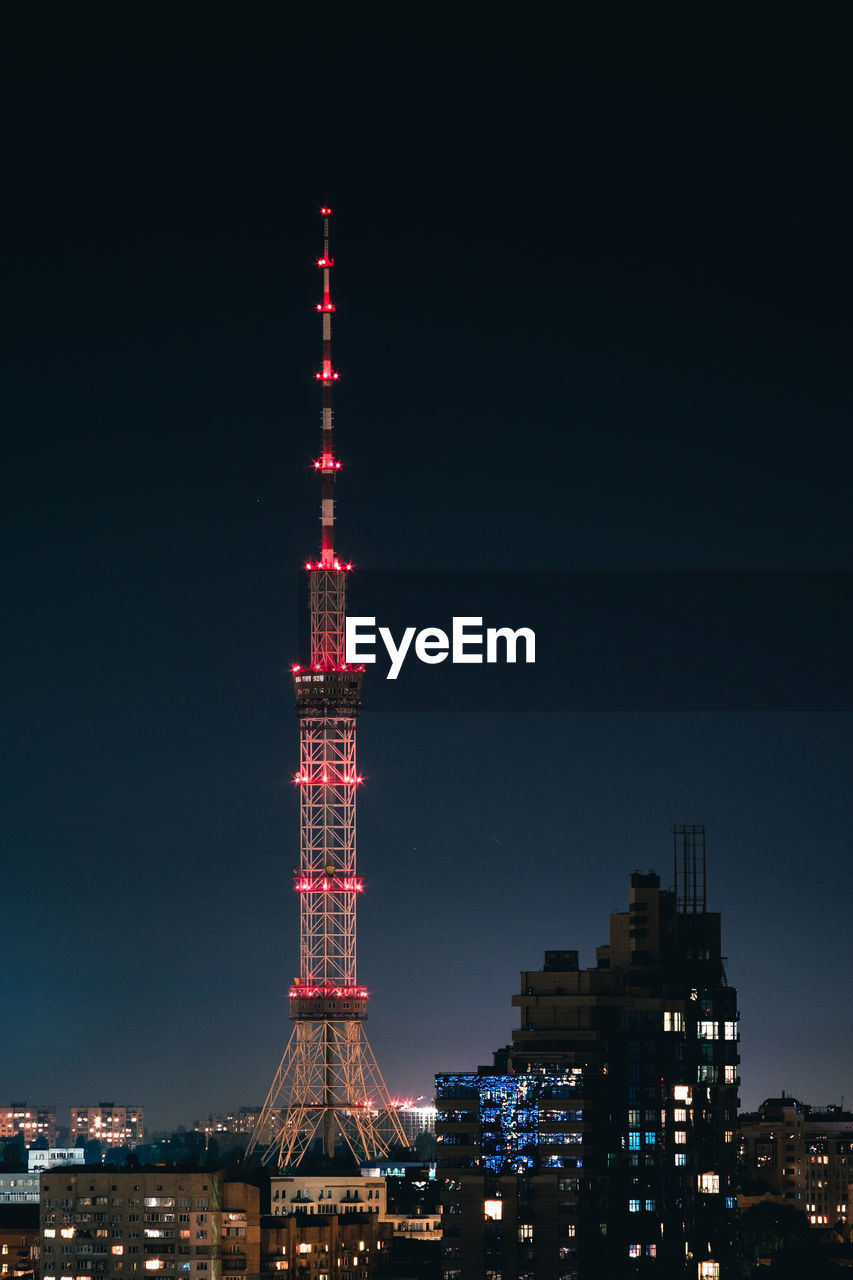 Illuminated communications tower in city against sky at night
