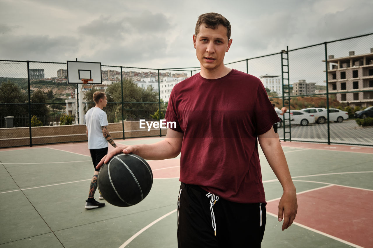 Young adult caucasian man plays basketball at outdoor sports court in the evening