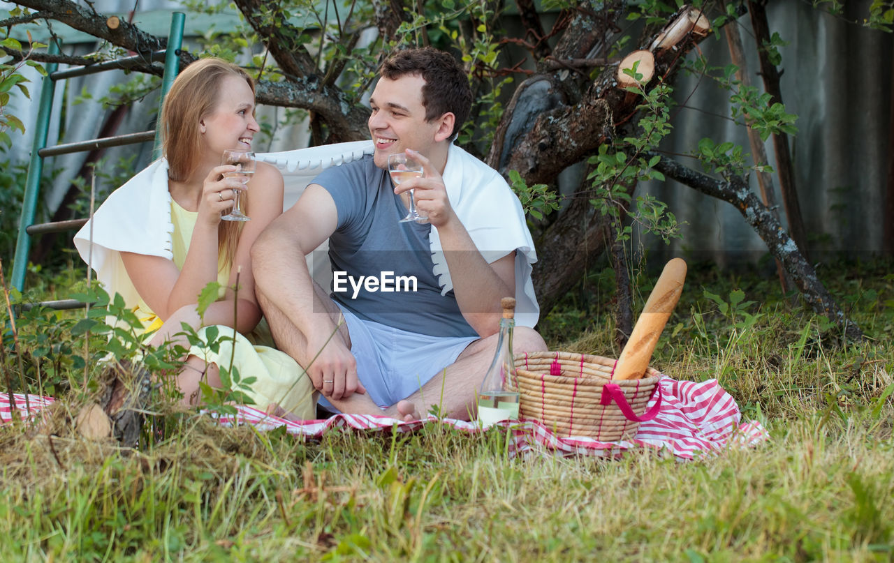 Smiling couple drinking white wine during picnic in garden