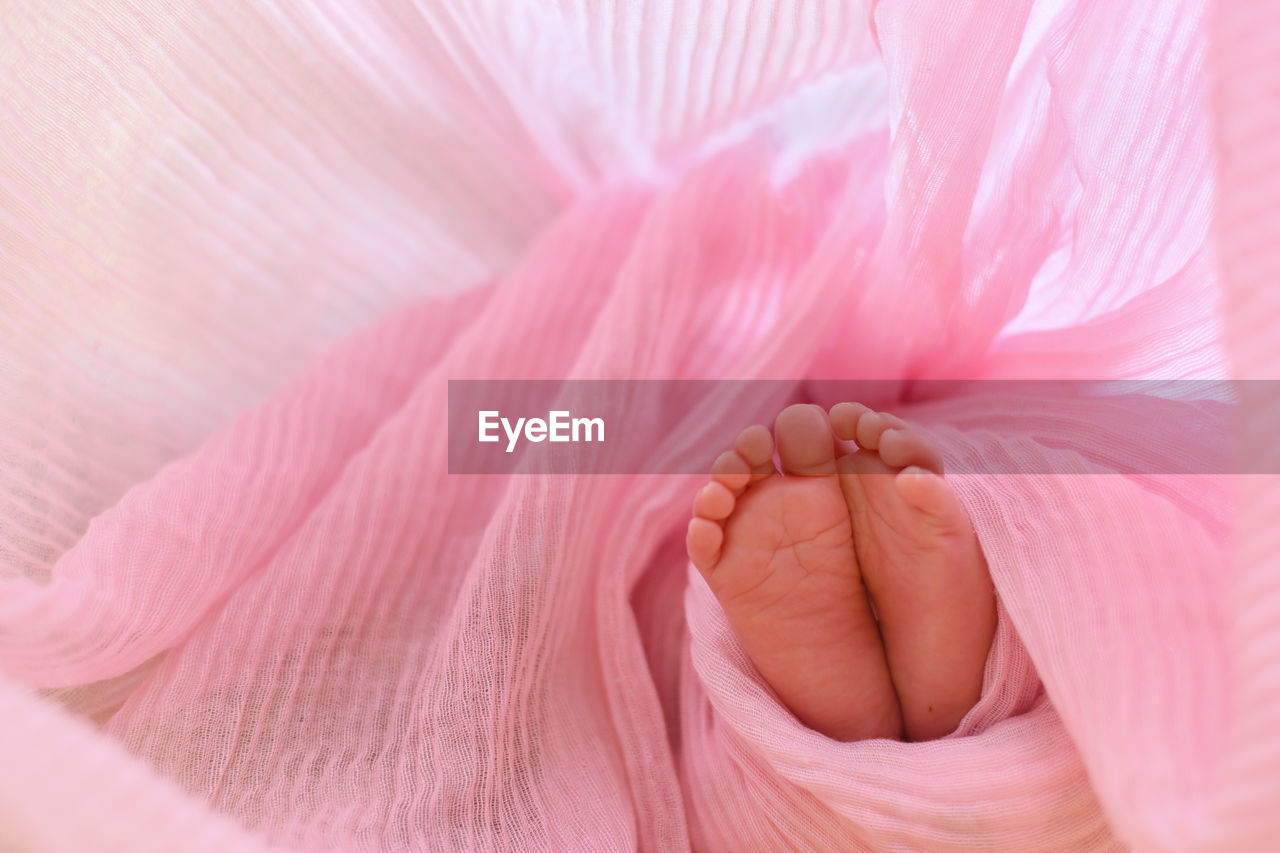 Low section of baby in pink blanket on bed at home