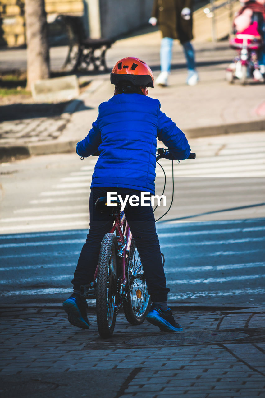 REAR VIEW OF SENIOR MAN RIDING BICYCLE ON STREET
