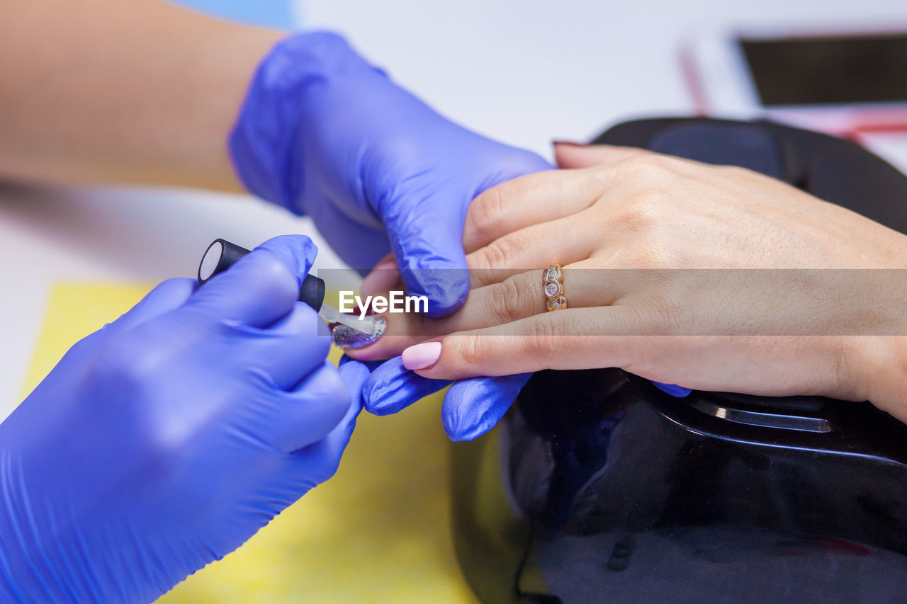 Close-up manicure master with sterile blue gloves paints nails with protective varnish to a woman 