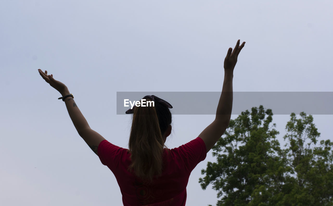 Rear view of woman with arms raised standing against clear sky