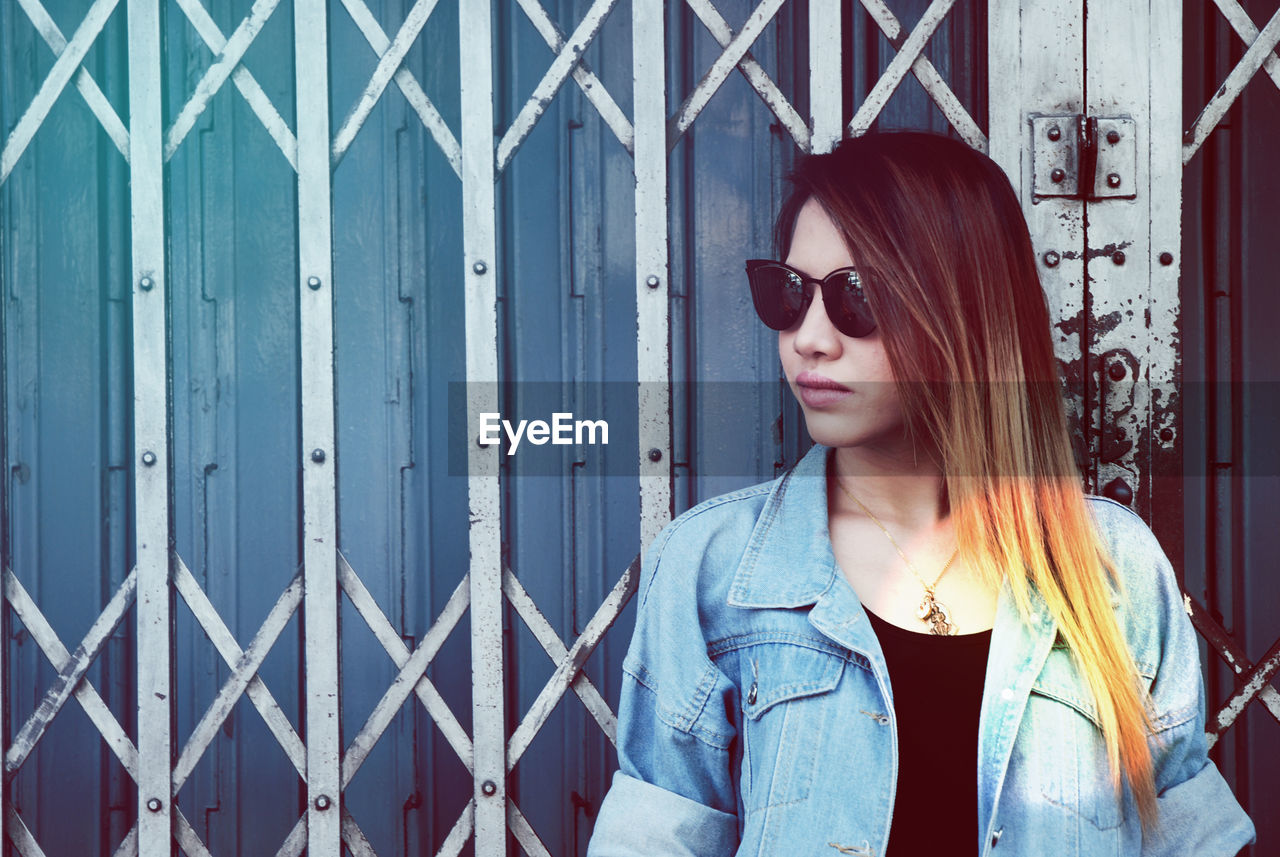 Woman looking away while standing against shutter