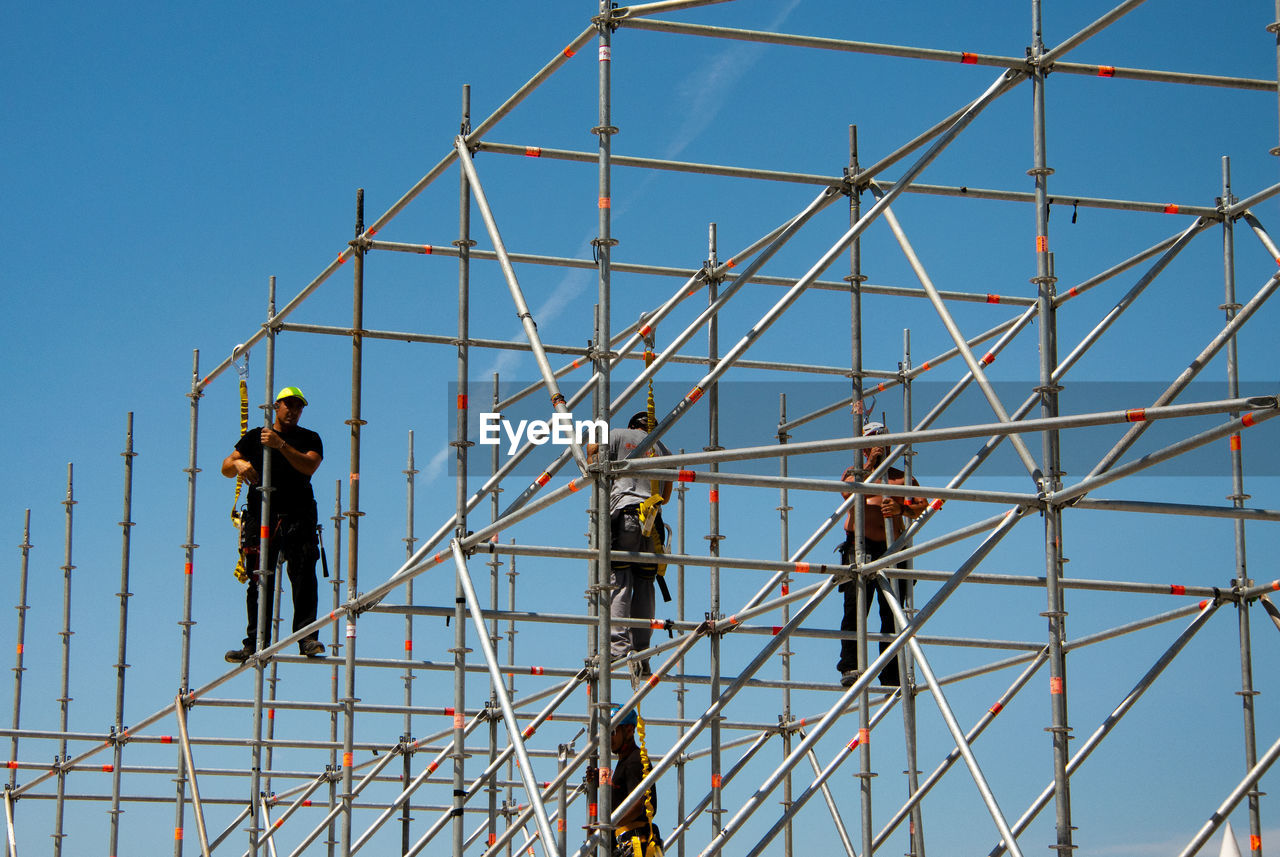 MEN WORKING AT CONSTRUCTION SITE AGAINST CLEAR BLUE SKY