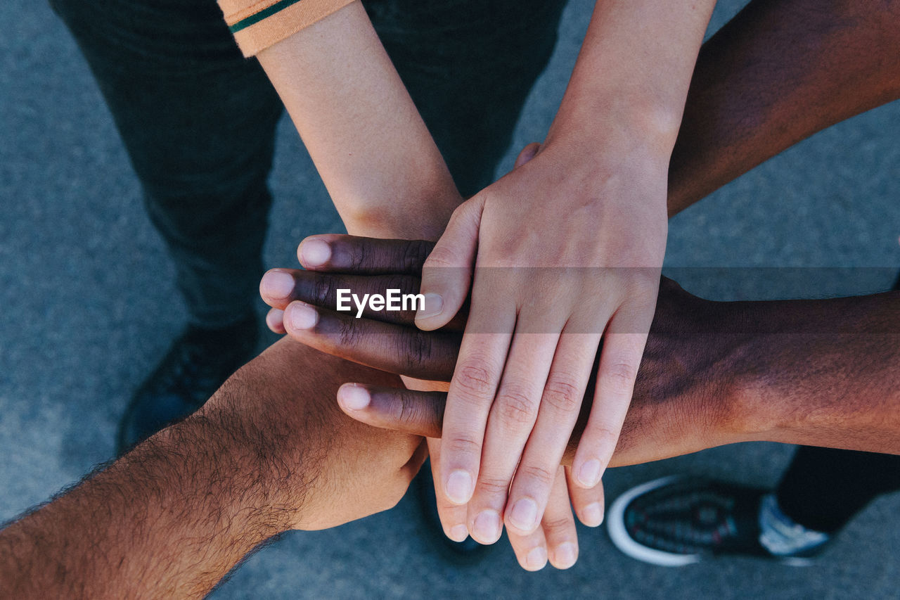 From above cropped unrecognizable african american people putting hands together standing on the street