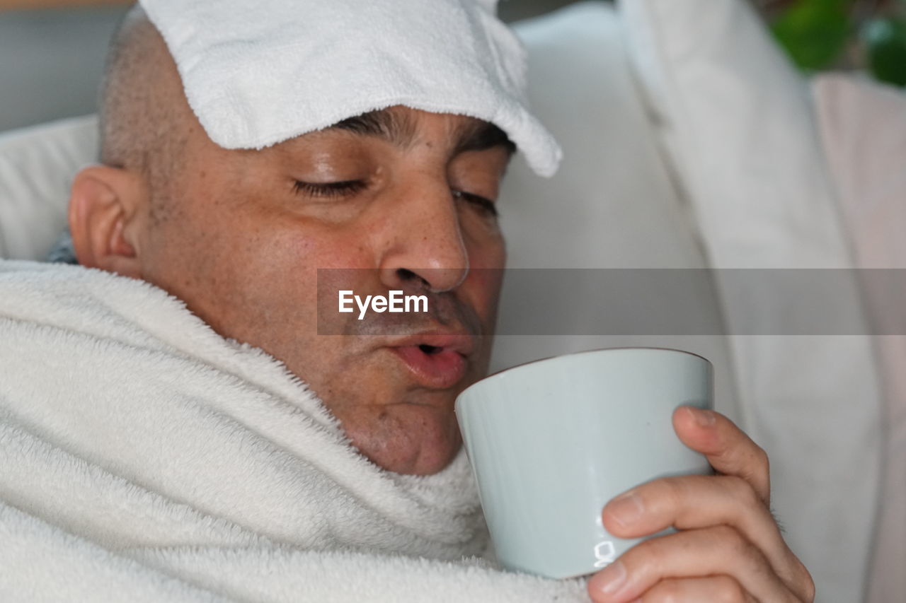 Man suffering from headache having coffee on bed at home