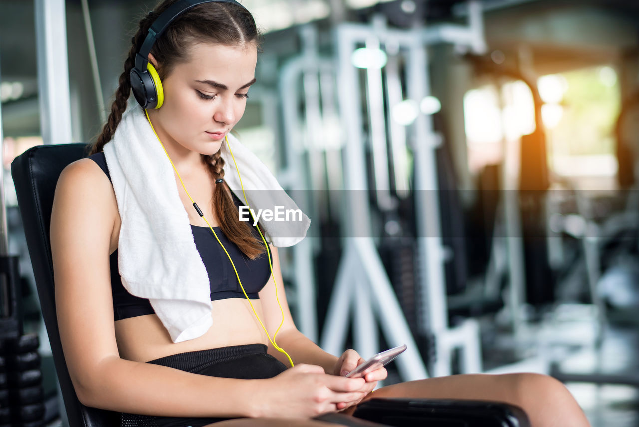 Woman using smart phone while sitting in gym