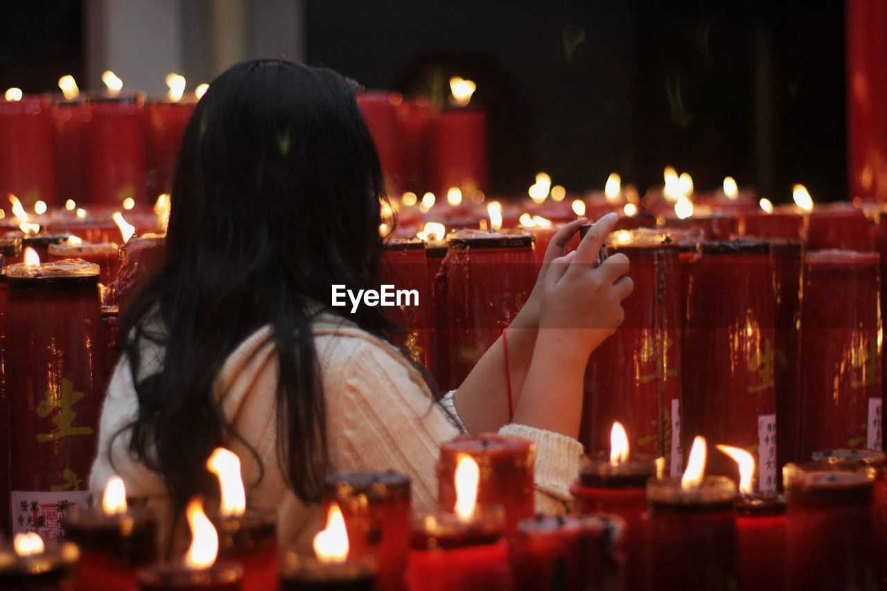 Rear view of woman against illuminated candles in temple