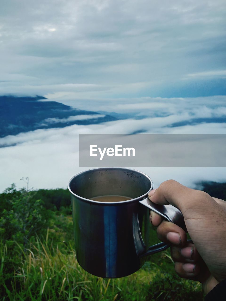 Midsection of person holding coffee cup against sky