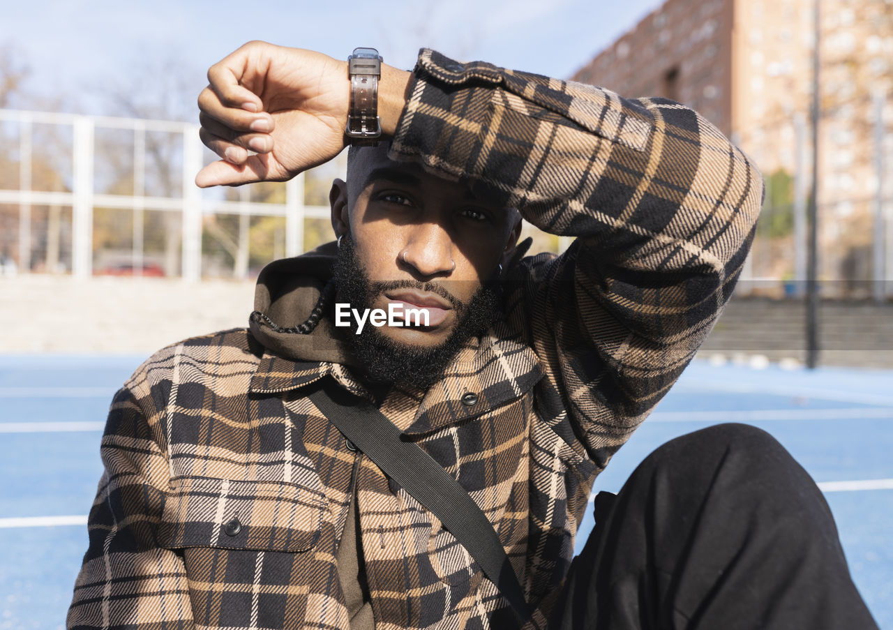 Young man with blank expression shielding eyes in sports court on sunny day