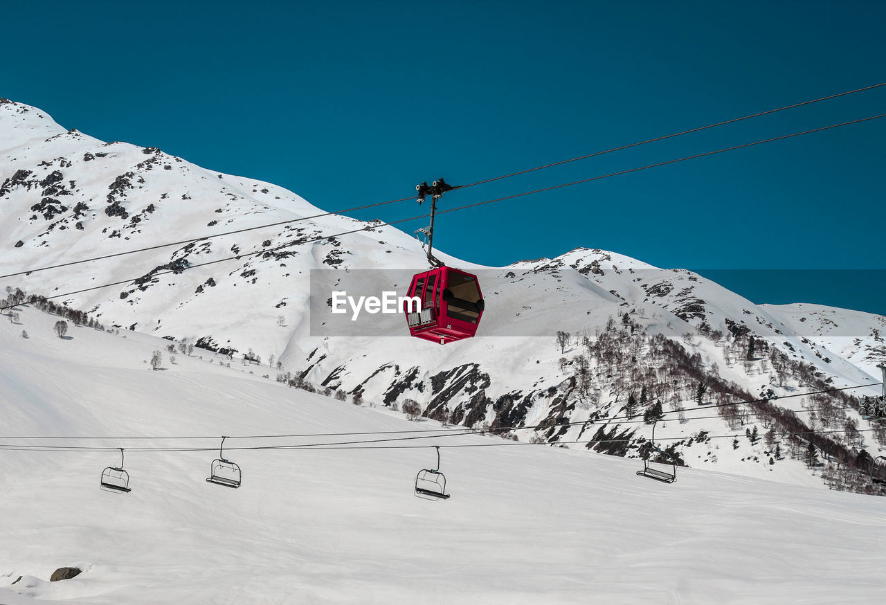 LOW ANGLE VIEW OF OVERHEAD CABLE CAR AGAINST SNOWCAPPED MOUNTAINS