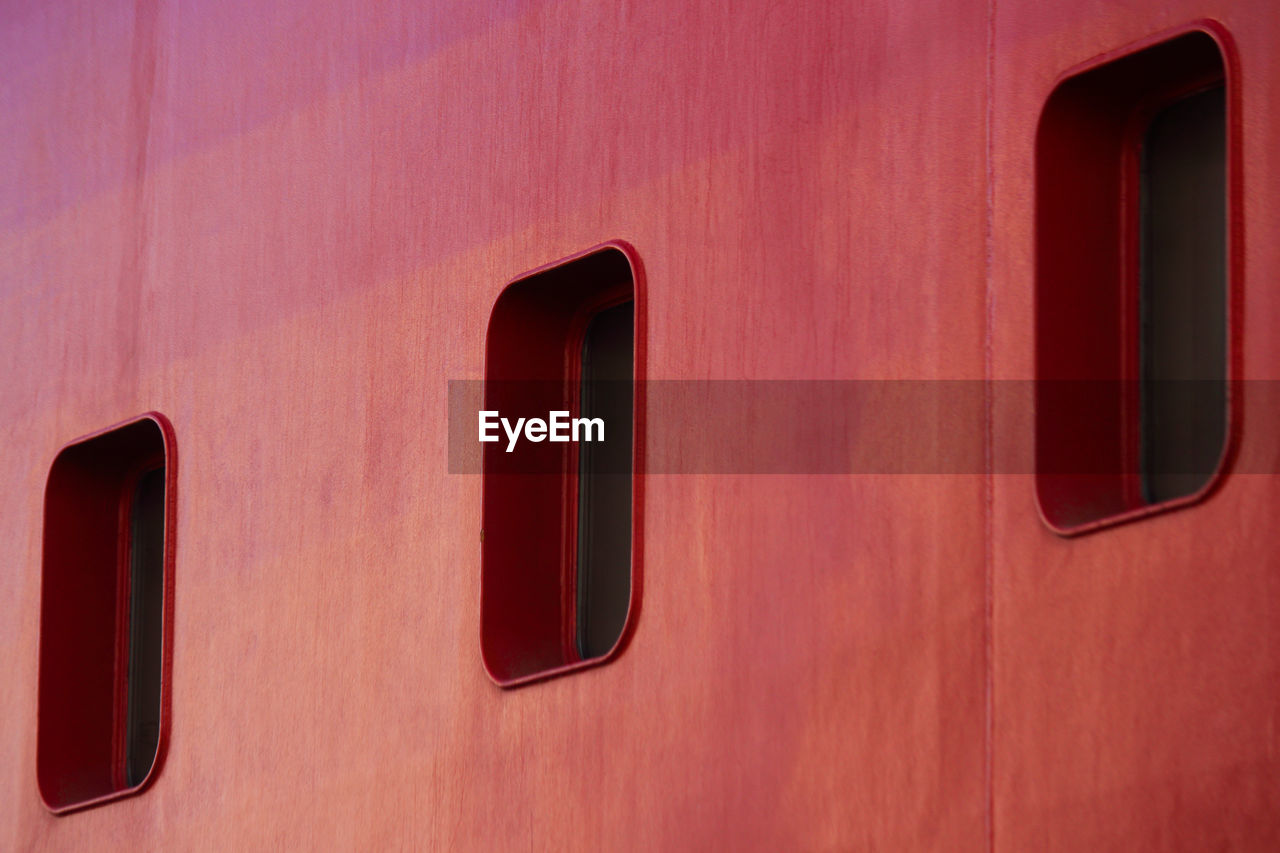 Three rectangular portholes on a red ship hull