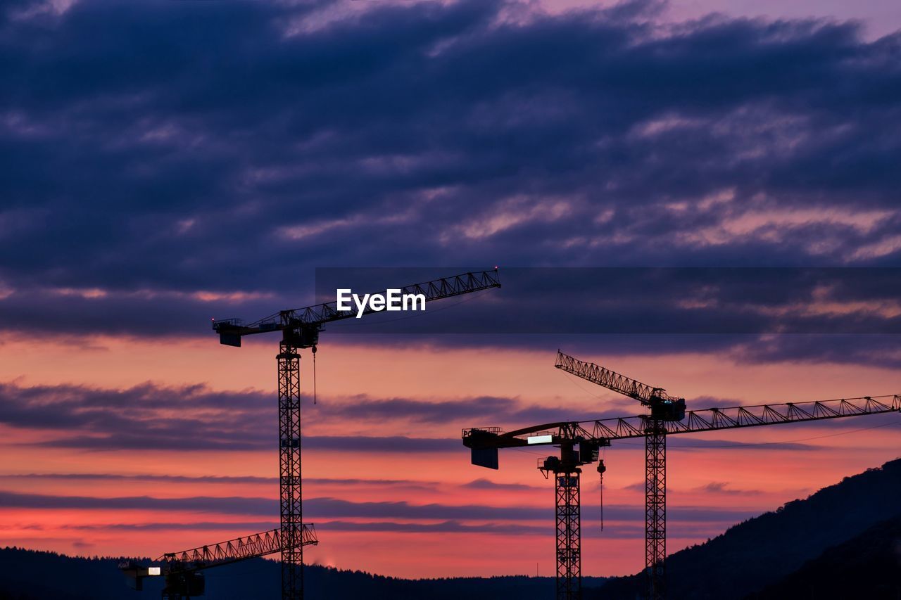Low angle view of silhouette cranes against sky at sunset