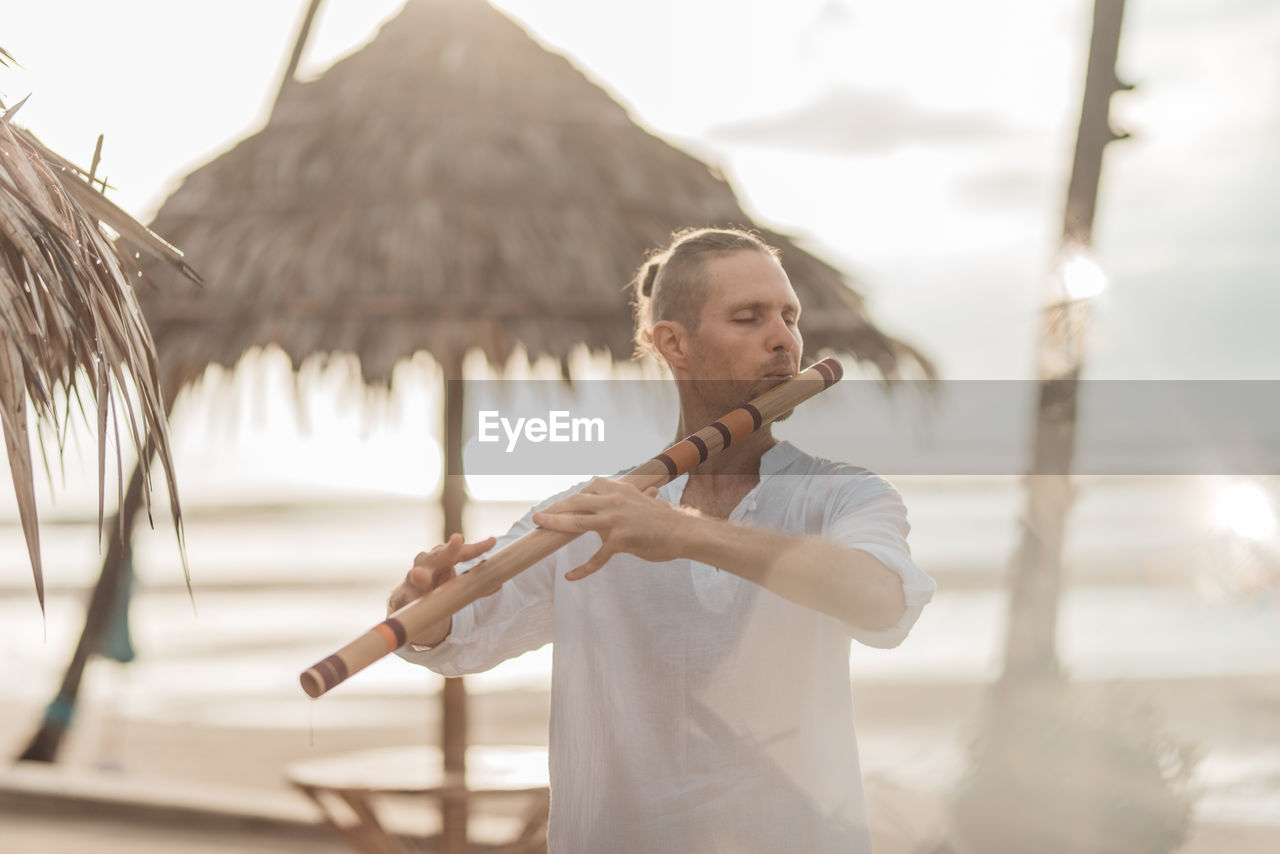 Man playing wind instrument on the beach at sunrise